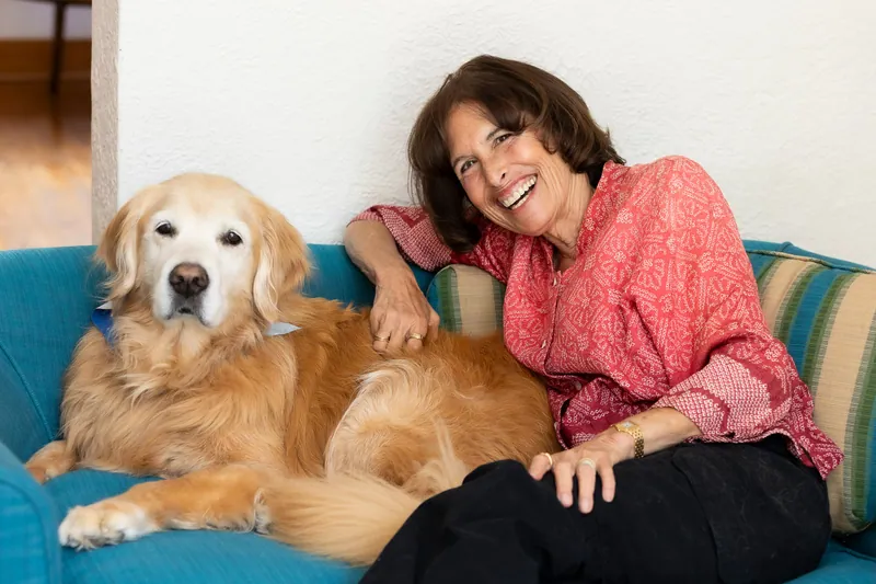 Sue Himmelrich laughing on a sofa beside Katie, her golden retriever.