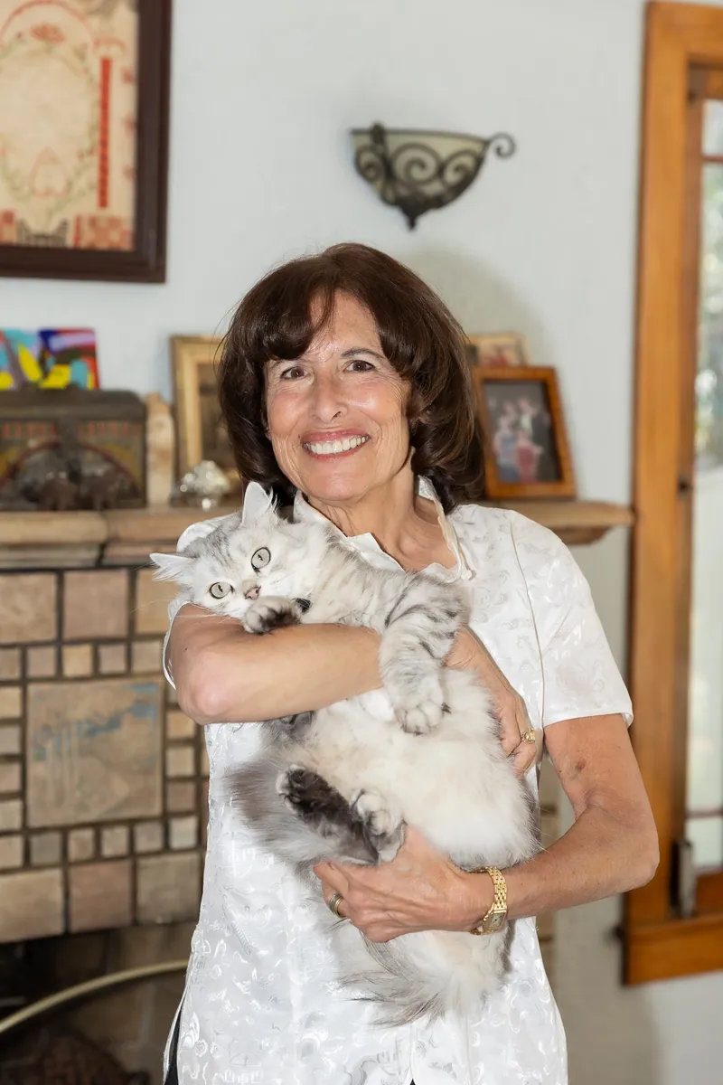 Sue Himmelrich smiling at home, holding Coco, her fluffy silver cat.